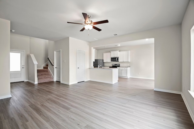unfurnished living room with stairs, wood finished floors, baseboards, and a ceiling fan