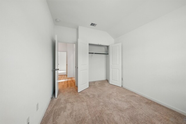 unfurnished bedroom featuring lofted ceiling, a closet, light colored carpet, and visible vents