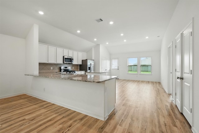 kitchen with light stone countertops, a sink, white cabinets, a peninsula, and appliances with stainless steel finishes