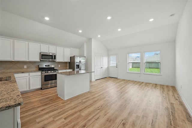 kitchen featuring decorative backsplash, a kitchen island, appliances with stainless steel finishes, white cabinetry, and vaulted ceiling