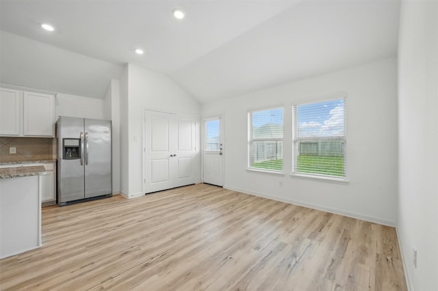 kitchen featuring lofted ceiling, white cabinetry, stainless steel refrigerator with ice dispenser, light wood-type flooring, and backsplash