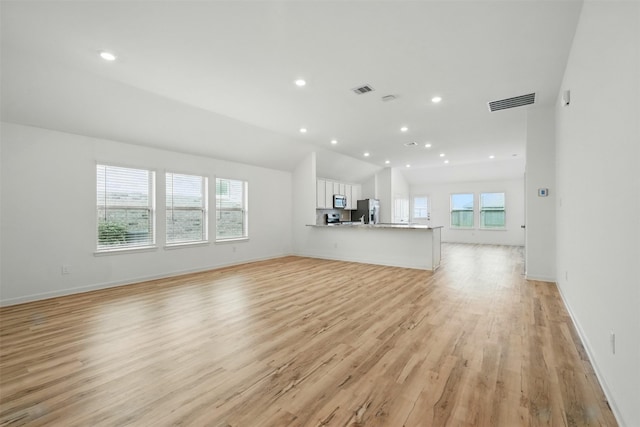 unfurnished living room featuring light wood finished floors, a wealth of natural light, and visible vents