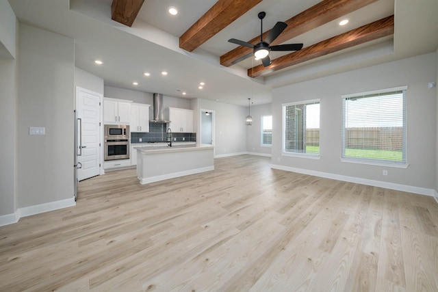 unfurnished living room featuring ceiling fan, baseboards, light wood-style floors, and beamed ceiling