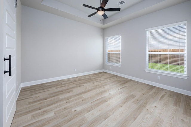 empty room with baseboards, a ceiling fan, light wood finished floors, and a raised ceiling