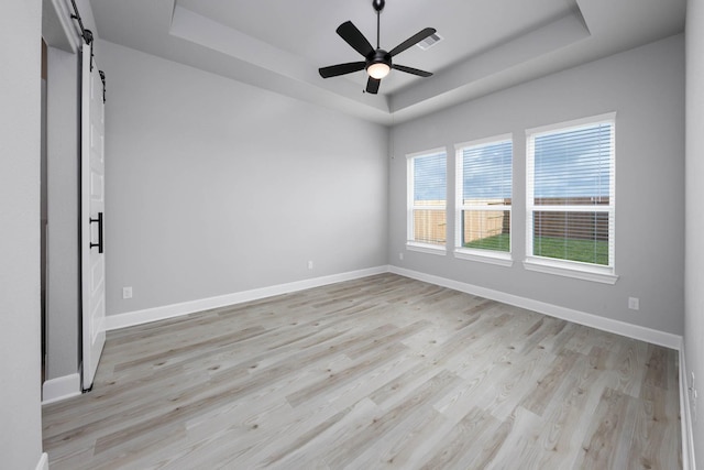 unfurnished room featuring a barn door, a raised ceiling, baseboards, and light wood-type flooring