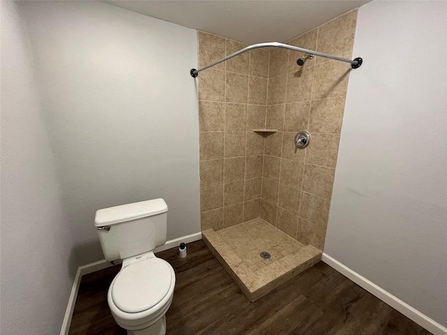 bathroom featuring toilet, wood finished floors, baseboards, and a tile shower