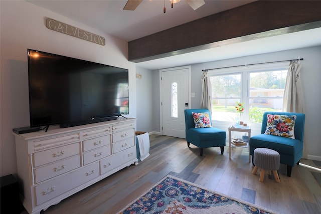 living room with a ceiling fan, beam ceiling, baseboards, and wood finished floors