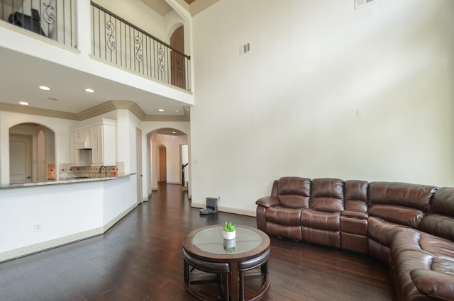 living room with dark wood-style flooring, a high ceiling, arched walkways, baseboards, and visible vents
