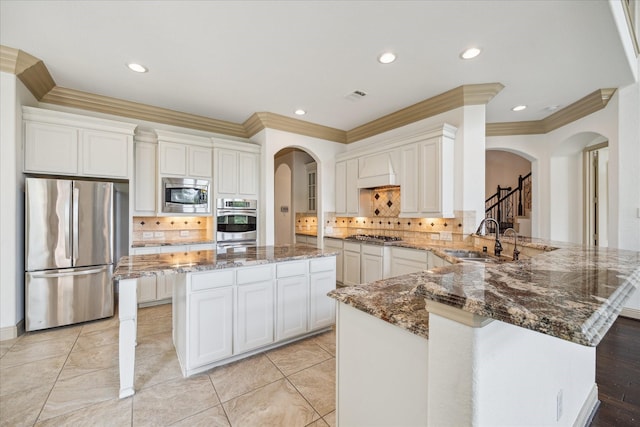 27 Tioga Pl, The Woodlands, TX 77375 - kitchen featuring stainless steel appliances, arched walkways, a sink, crown molding, and a peninsula