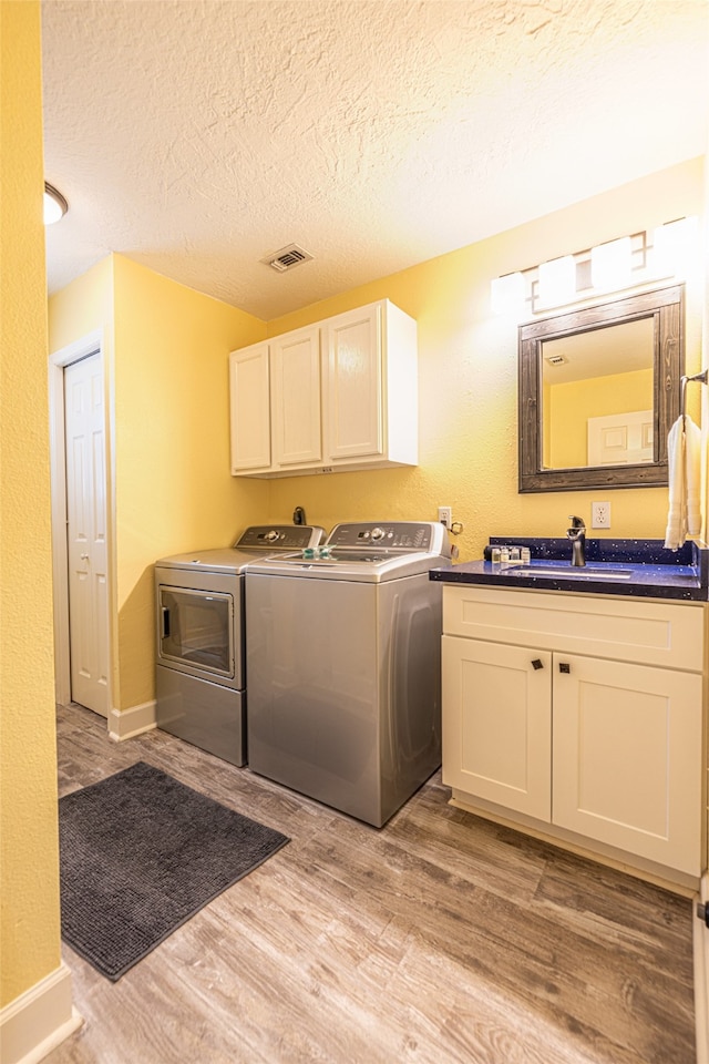 4206 Seabird Dr, Galveston, TX 77554 - washroom featuring washing machine and clothes dryer, cabinet space, light wood-type flooring, and a textured ceiling