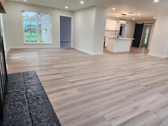 unfurnished living room featuring a sink, a barn door, baseboards, light wood-style floors, and recessed lighting