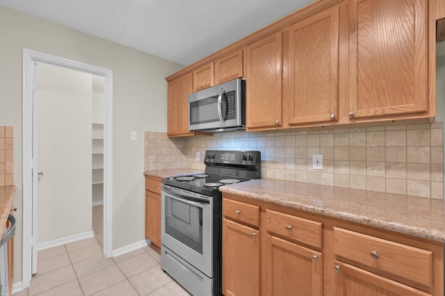 kitchen with light tile patterned flooring, tasteful backsplash, light stone countertops, stainless steel appliances, and baseboards
