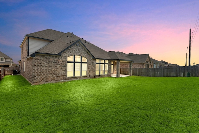 6518 Fairway Glen Ln, Katy, TX 77493 - back of property at dusk featuring a patio, a shingled roof, a fenced backyard, a lawn, and brick siding