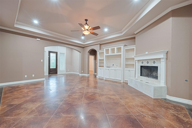 unfurnished living room featuring a raised ceiling, arched walkways, baseboards, and a ceiling fan