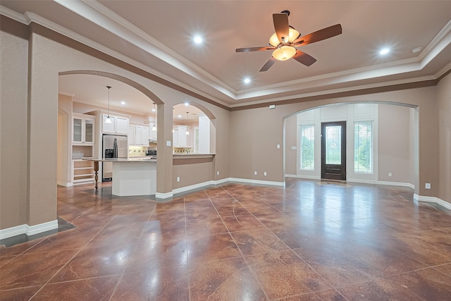 unfurnished living room featuring baseboards, arched walkways, ornamental molding, ceiling fan, and a tray ceiling