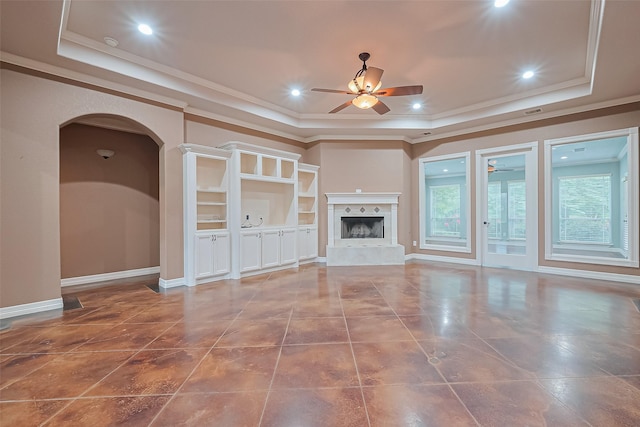 unfurnished living room featuring a tray ceiling, ceiling fan, and arched walkways