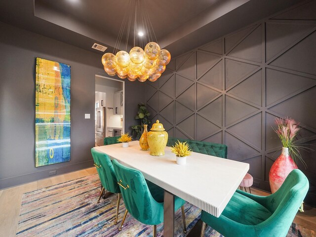 dining room featuring a chandelier, baseboards, a tray ceiling, a decorative wall, and wood finished floors