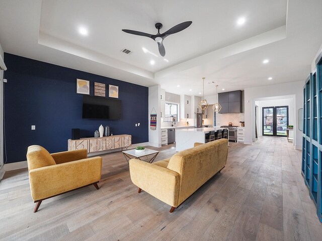 living room with a raised ceiling, recessed lighting, light wood-style floors, ceiling fan, and baseboards