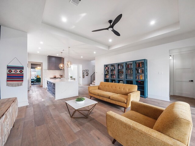 living area with a raised ceiling, light wood-style flooring, a ceiling fan, baseboards, and recessed lighting