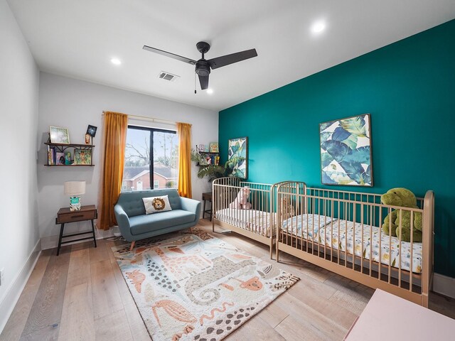 bedroom with wood finished floors, an accent wall, recessed lighting, a ceiling fan, and a crib