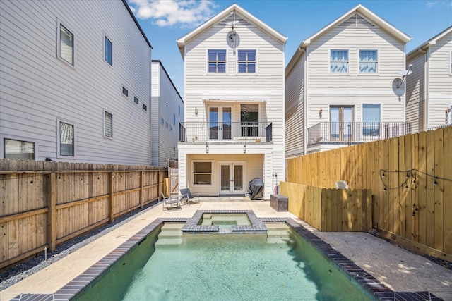 rear view of property with a patio, french doors, a pool with connected hot tub, a fenced backyard, and a balcony