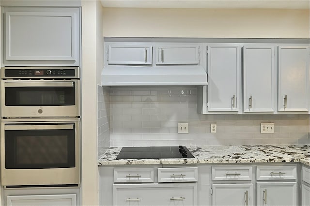 kitchen featuring backsplash, stainless steel double oven, light stone countertops, white cabinets, and black electric stovetop