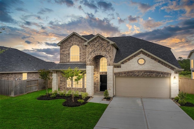 french country inspired facade with fence, an attached garage, a lawn, driveway, and a shingled roof