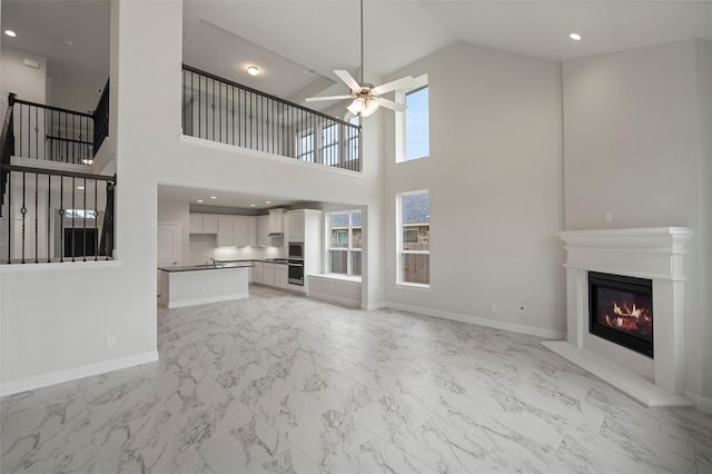 unfurnished living room with marble finish floor, a glass covered fireplace, baseboards, and ceiling fan