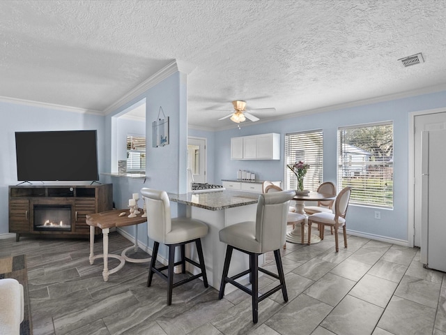 dining space featuring visible vents, baseboards, ornamental molding, ceiling fan, and a glass covered fireplace