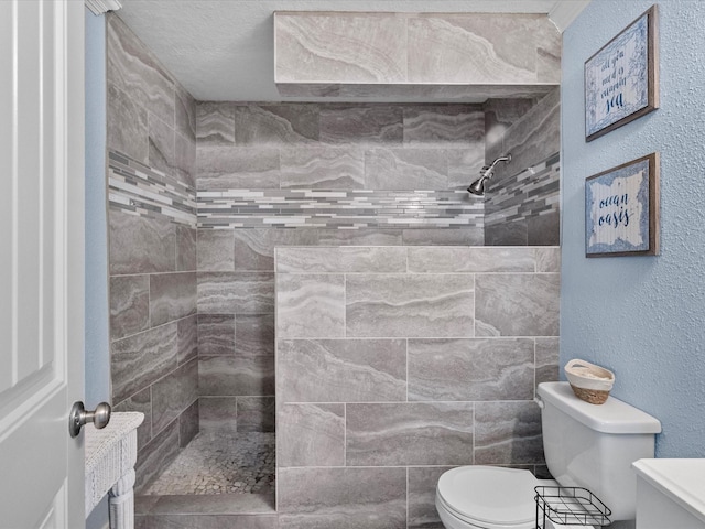 bathroom with toilet, a textured wall, and a tile shower