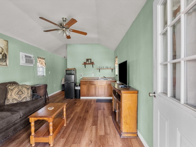 living area featuring a wall mounted AC, vaulted ceiling, baseboards, a ceiling fan, and wood finished floors