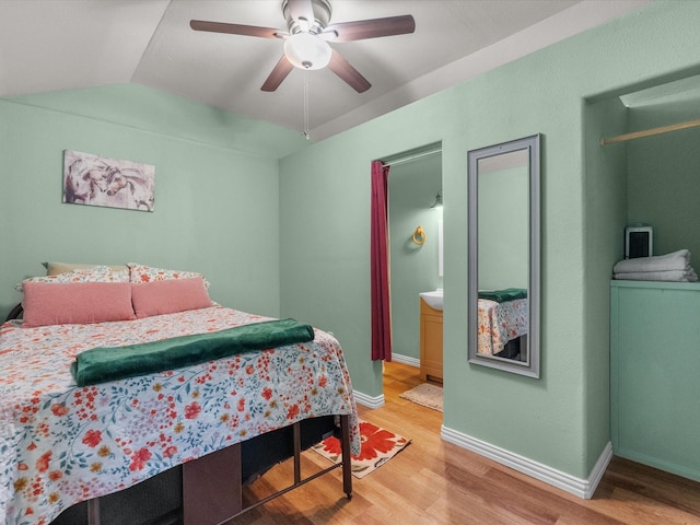 bedroom featuring ensuite bathroom, baseboards, ceiling fan, light wood-type flooring, and vaulted ceiling