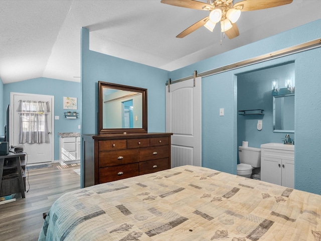 bedroom featuring lofted ceiling, a textured ceiling, a barn door, ceiling fan, and wood finished floors