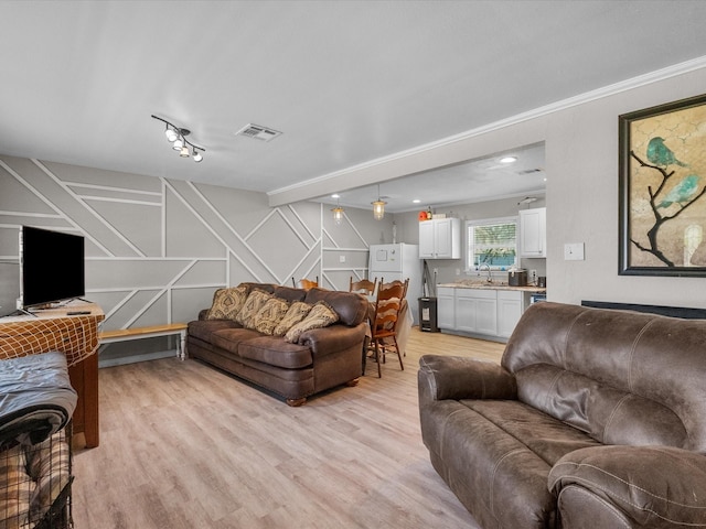 living area with crown molding, stairway, light wood finished floors, a decorative wall, and visible vents