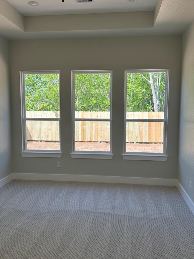 carpeted empty room featuring visible vents, baseboards, and a raised ceiling