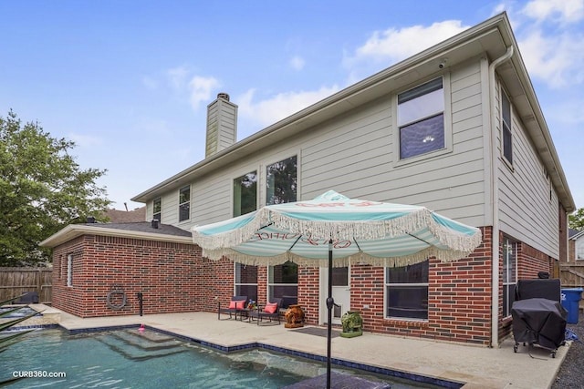 back of property with a fenced in pool, a patio, brick siding, and a chimney