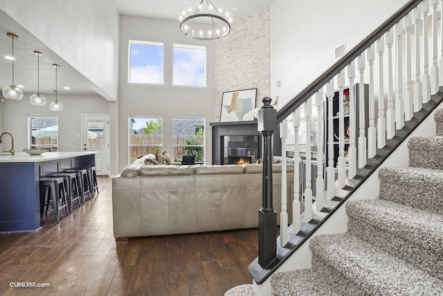 living area featuring a high ceiling, an inviting chandelier, dark wood-style floors, stairs, and a large fireplace