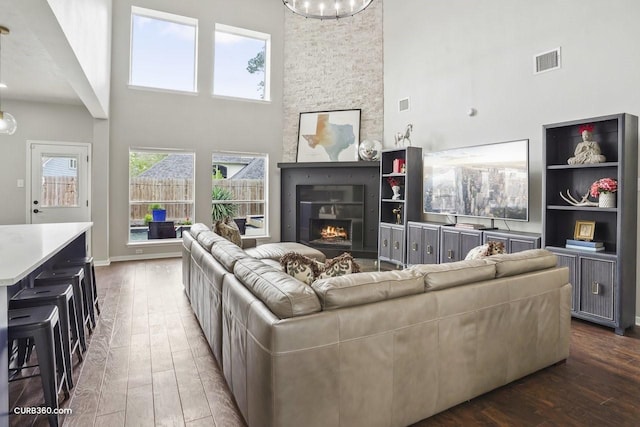 living area featuring a towering ceiling, visible vents, hardwood / wood-style flooring, and a stone fireplace