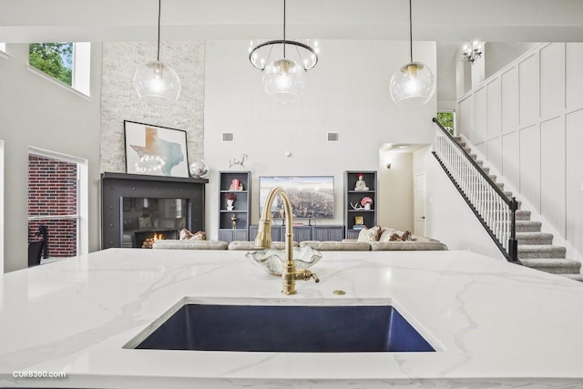 kitchen with a sink, open floor plan, a glass covered fireplace, and light stone countertops