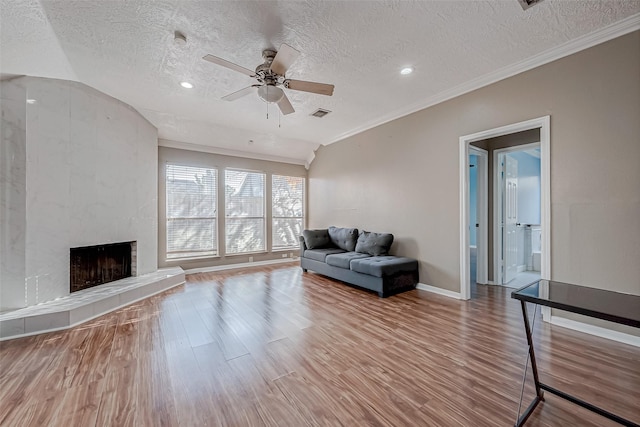 living area featuring crown molding, a premium fireplace, a textured ceiling, a ceiling fan, and wood finished floors
