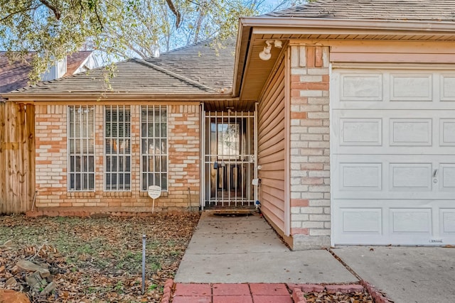 doorway to property with brick siding, a garage, and roof with shingles