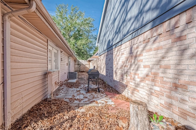 view of side of property featuring brick siding, fence, and a patio area