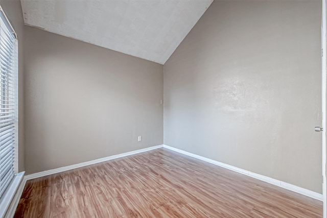 spare room featuring light wood-style flooring, baseboards, and vaulted ceiling