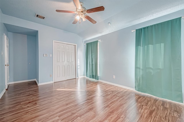 unfurnished room with visible vents, baseboards, wood finished floors, a ceiling fan, and vaulted ceiling