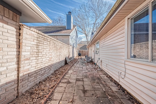 view of side of property featuring a fenced backyard, a patio, central air condition unit, and a chimney