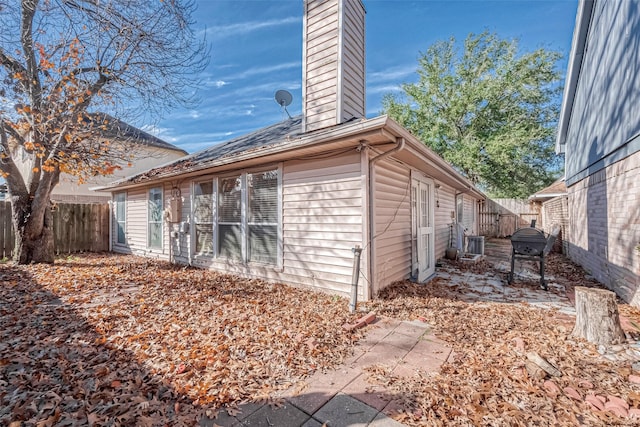 view of side of home with central air condition unit, a chimney, and fence