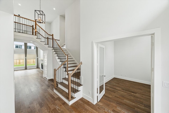 staircase featuring a high ceiling, a notable chandelier, wood finished floors, and baseboards