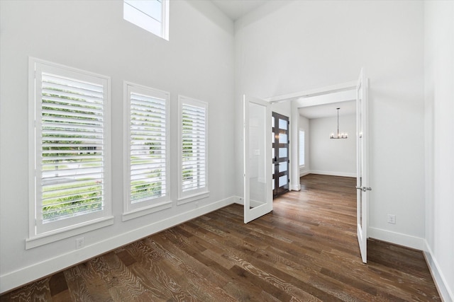 interior space with a high ceiling, baseboards, an inviting chandelier, and dark wood-style flooring