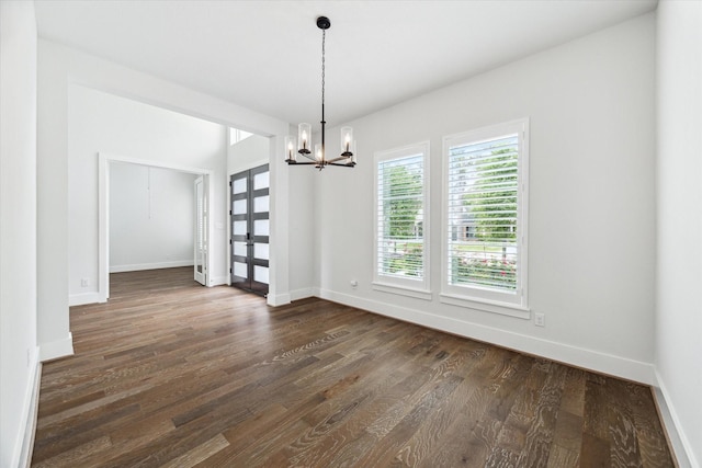 unfurnished dining area featuring dark wood-style flooring, a notable chandelier, and baseboards