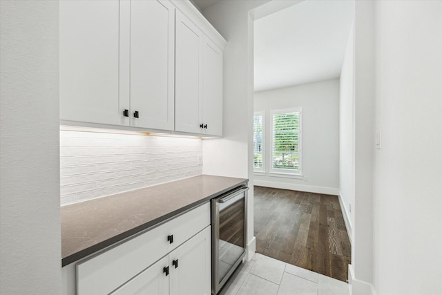 interior space with beverage cooler, light wood finished floors, a bar, baseboards, and decorative backsplash